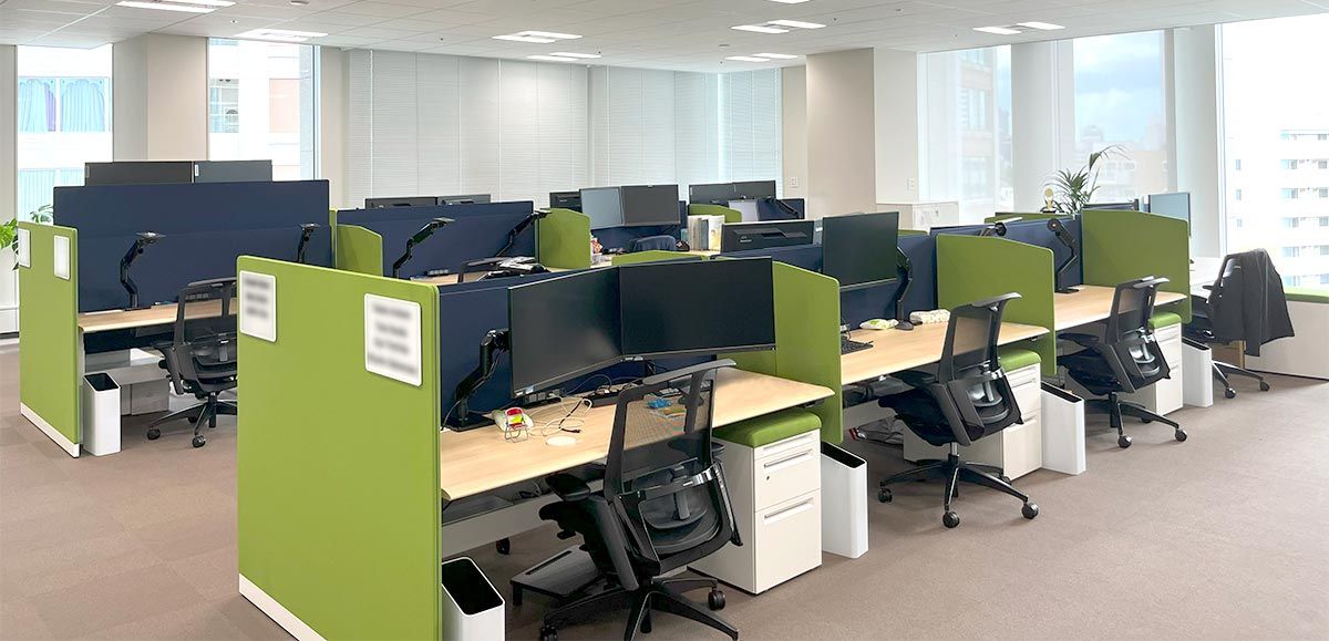 Two rows of cubicles with ergonomic chairs and large monitor setups.