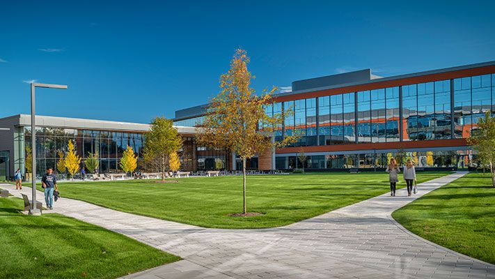 Sunny, grassy quad surrounded by modern brick and glass buildings.