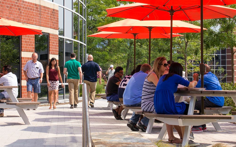 Patio seating area with tables with umbrellas and MathWorks staff in casual clothing.
