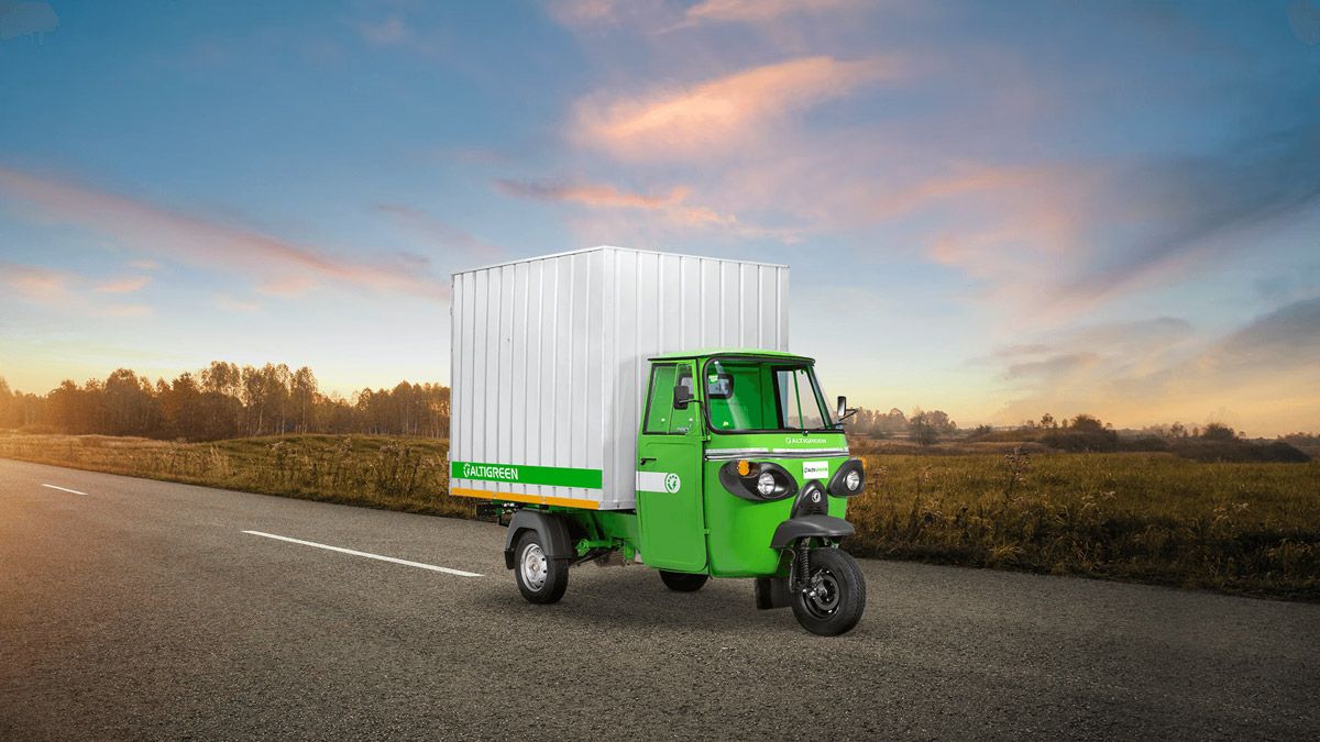 The three-wheeler electric cargo vehicle driving down a country road at sunset.