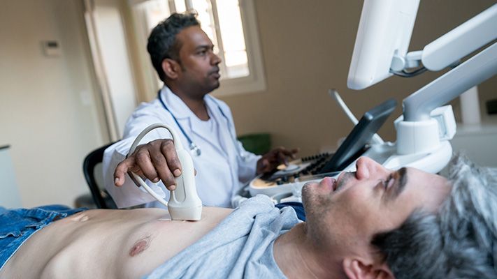Liegender Mann, der von einem Klinikmitarbeiter diagnostisch untersucht wird.